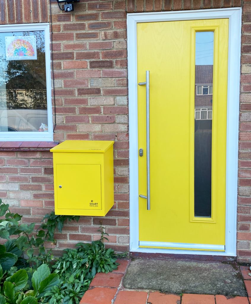 Medium yellow smart parcel box next to a yellow front door.